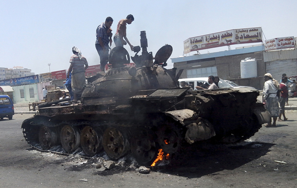 People stand on a tank that was burnt during clashes on a street in Yemen's southern port city of Aden on March 29, 2015. Source: REUTERS