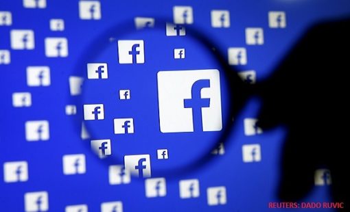 A man poses with a magnifier in front of a Facebook logo on display in this illustration taken in Sarajevo